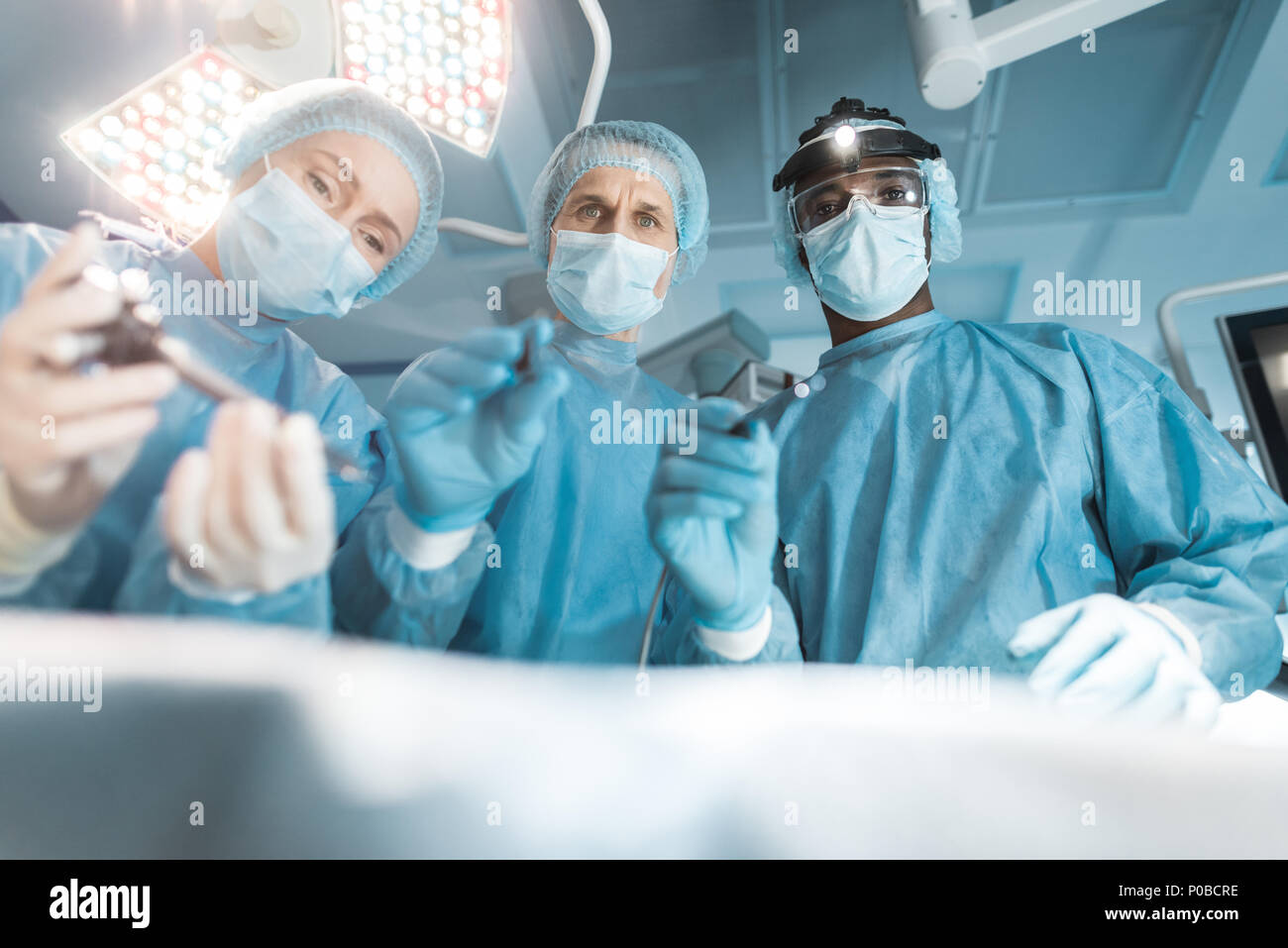 Vista dal basso dei chirurghi multiculturale guardando al paziente durante un intervento chirurgico Foto Stock