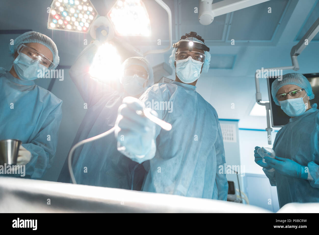 Vista dal basso dei chirurghi multiculturale guardando la fotocamera durante la chirurgia Foto Stock