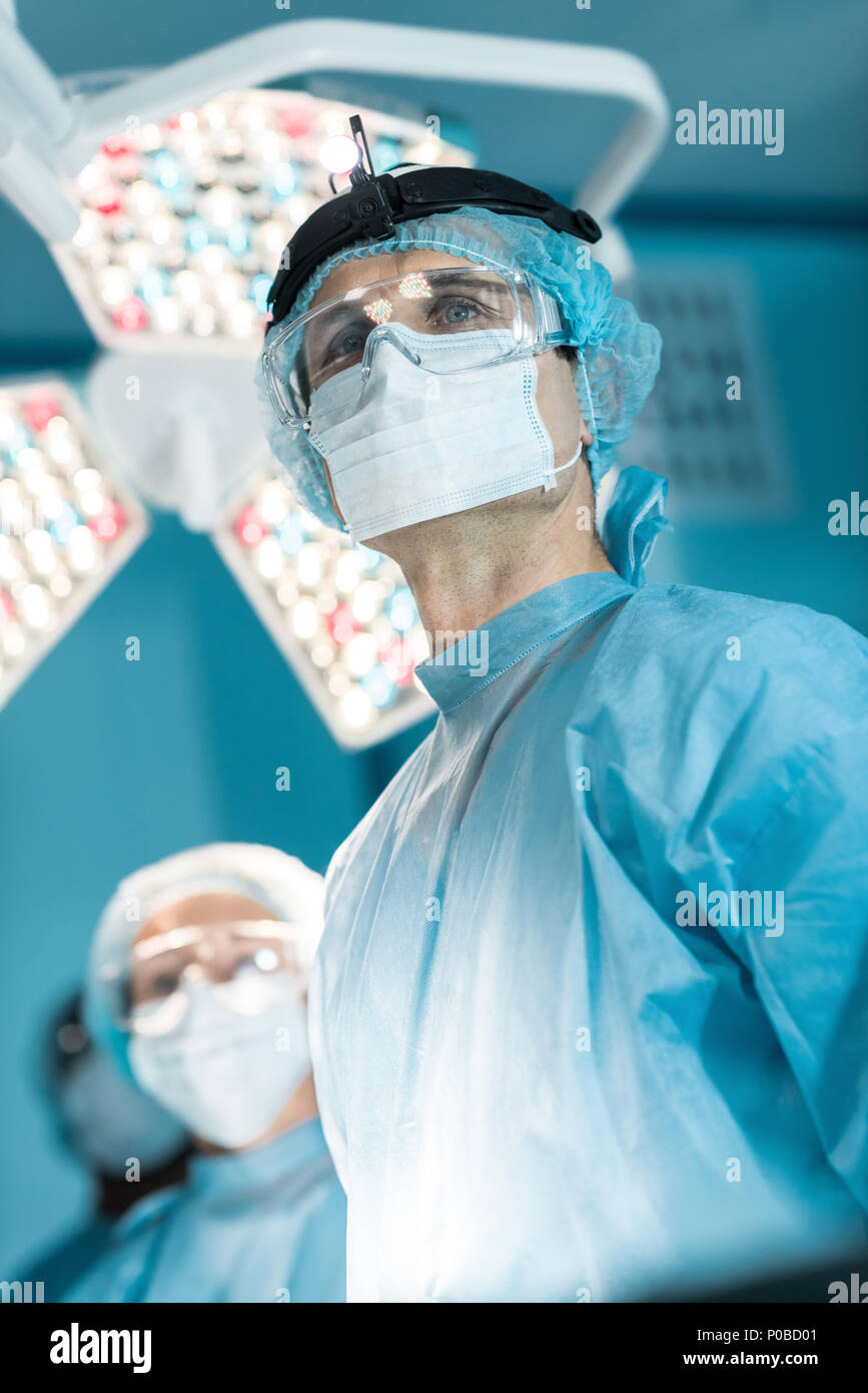 Vista dal basso del chirurgo nella maschera di medici che guarda lontano Foto Stock