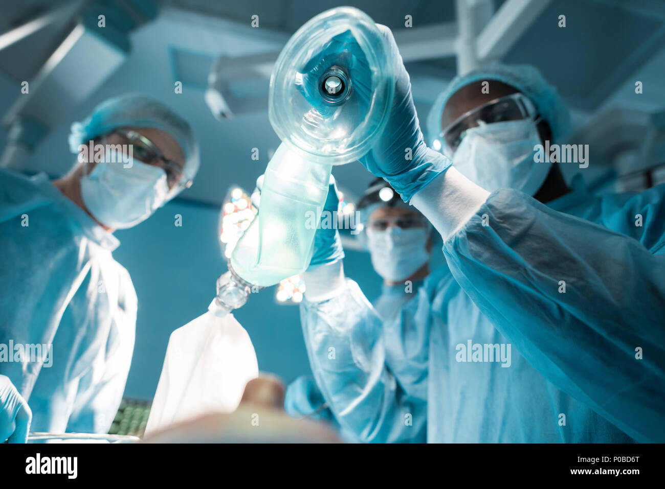 Vista dal basso del african american anestesista tenendo le maschere di ossigeno al di sopra di paziente in sala operatoria Foto Stock