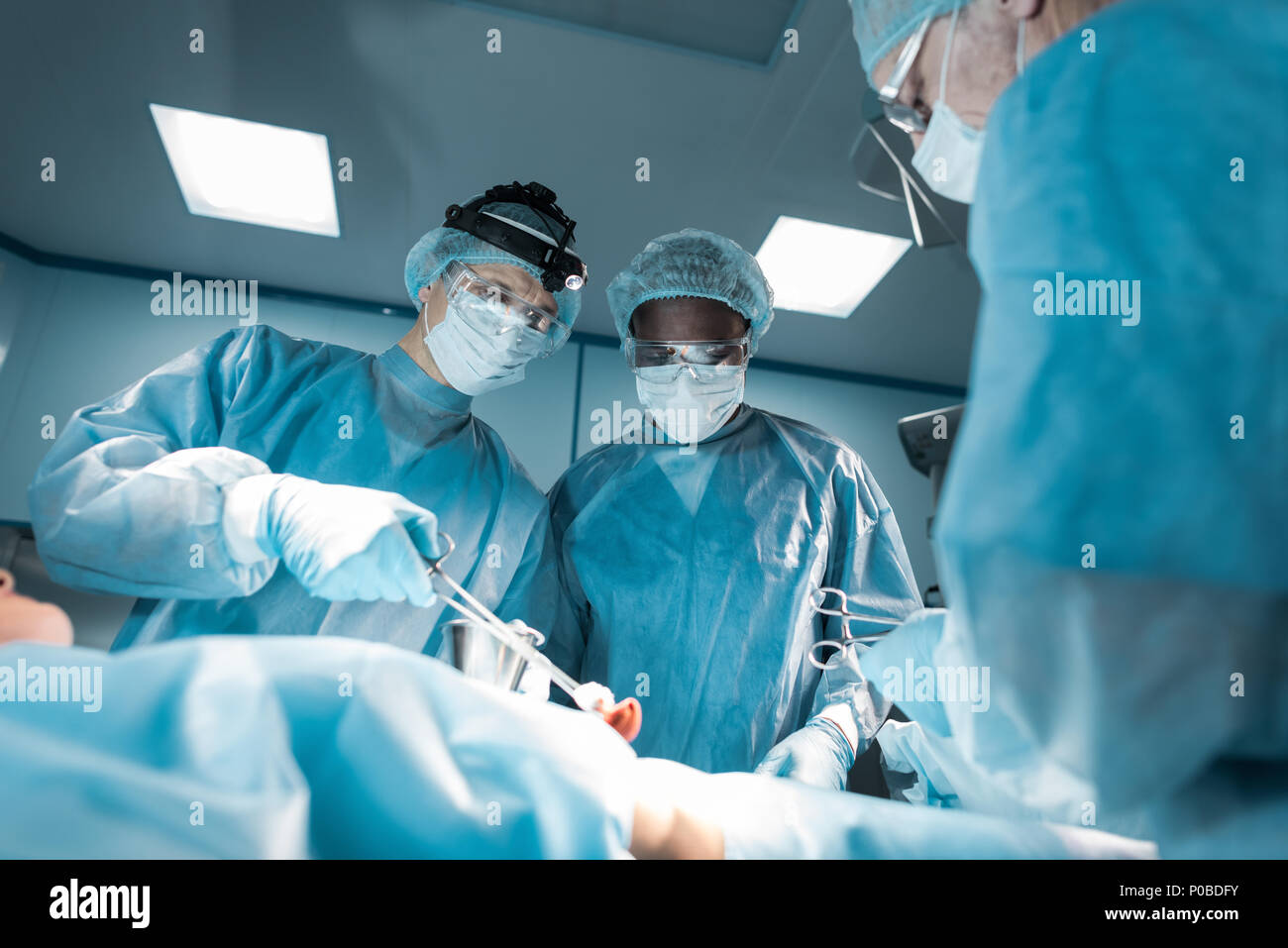 Vista dal basso dei chirurghi multiculturale e il paziente in sala operatoria Foto Stock