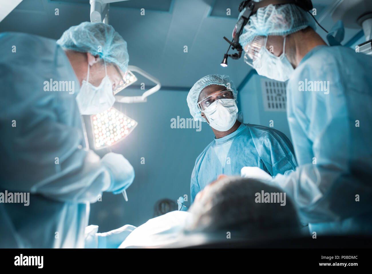 Vista dal basso dei chirurghi multiculturale operando il paziente in sala operatoria Foto Stock