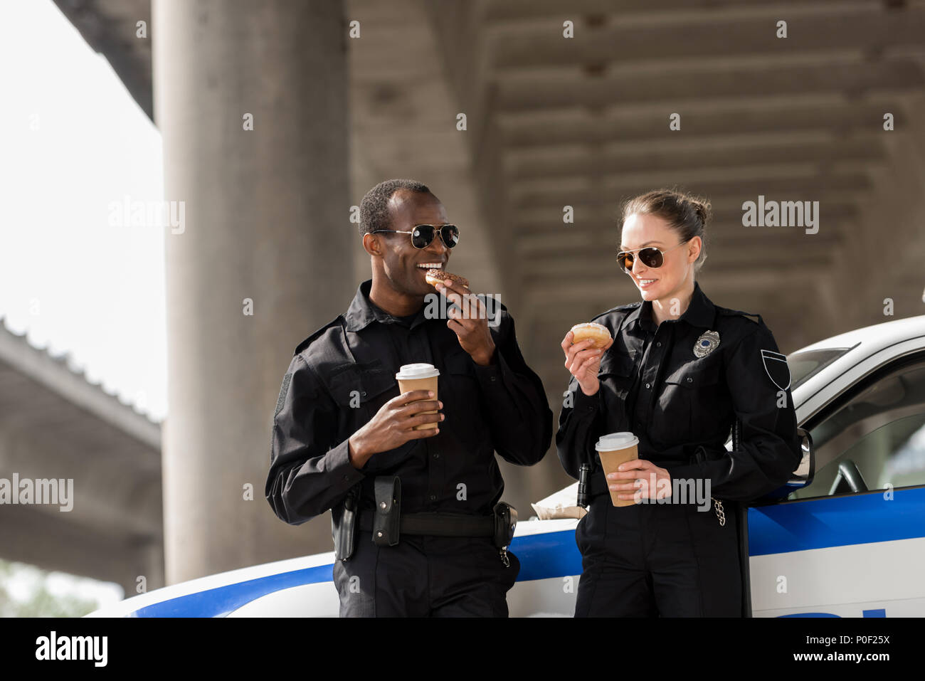 I giovani funzionari di polizia con caffè e ciambelle in piedi accanto a AUTO sotto il ponte Foto Stock