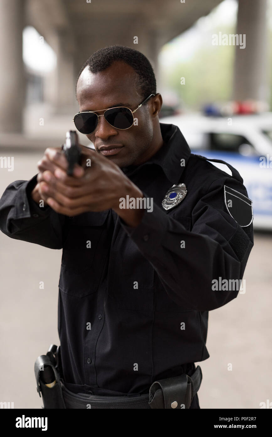 Giovane africana poliziotto americano in occhiali da sole mirando dalla  pistola Foto stock - Alamy