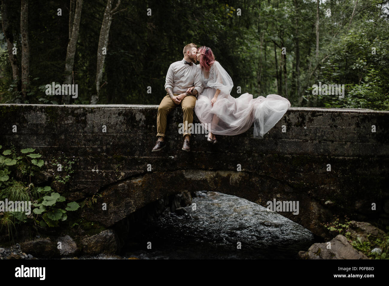 Bella giovani sposi kissing mentre è seduto sul ponte sopra il fiume di montagna nelle Alpi Foto Stock