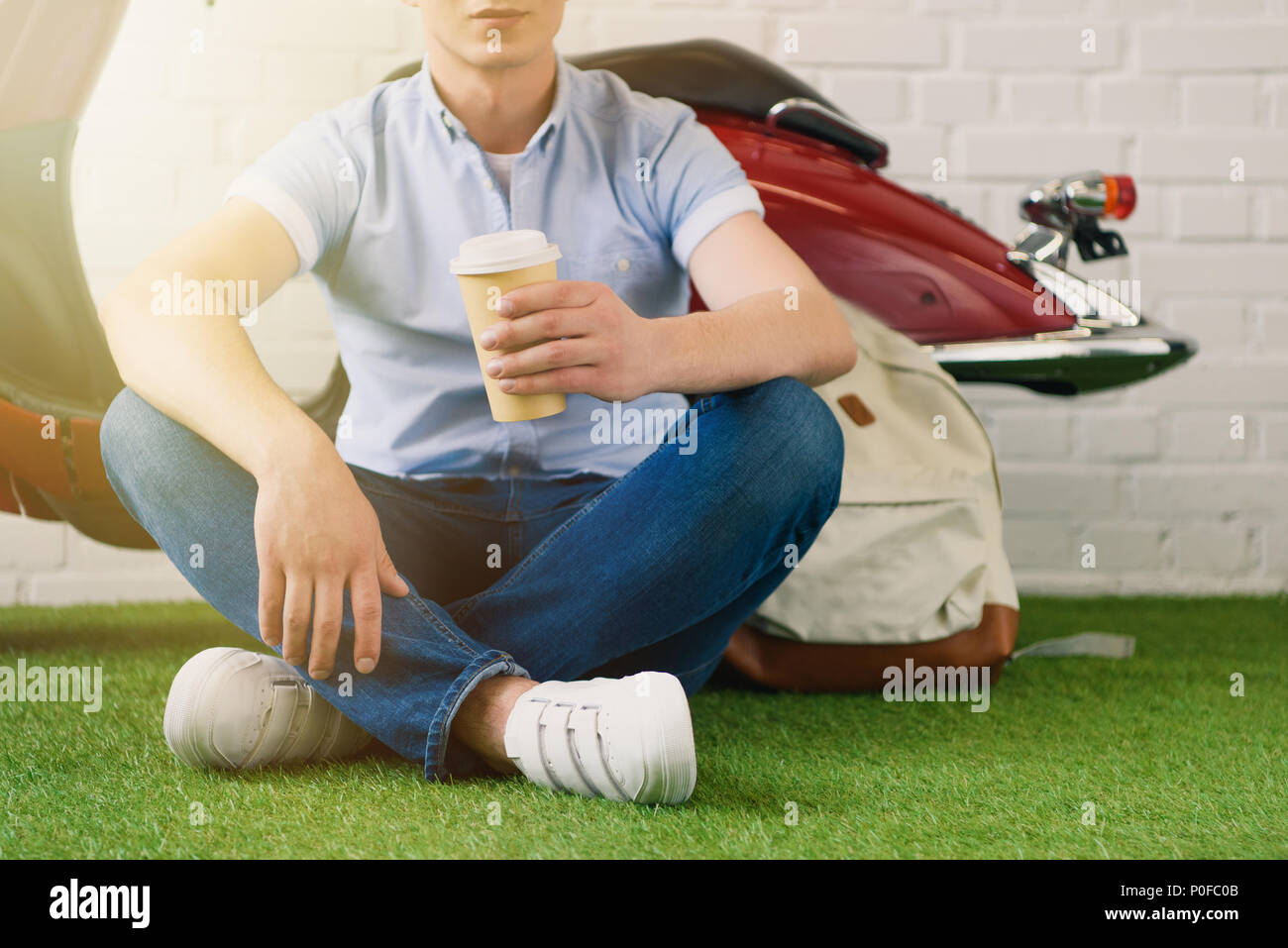 Ritagliato colpo di giovane con tazza di caffè a fo seduto davanti a scooter vintage Foto Stock