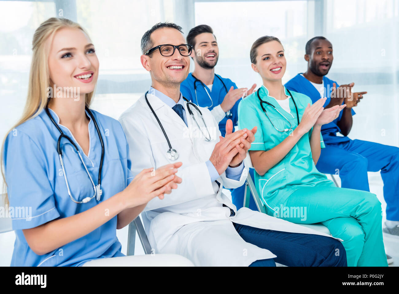 Team di medici seduti su sedie e battendo le mani mentre si ascolta la lezione Foto Stock