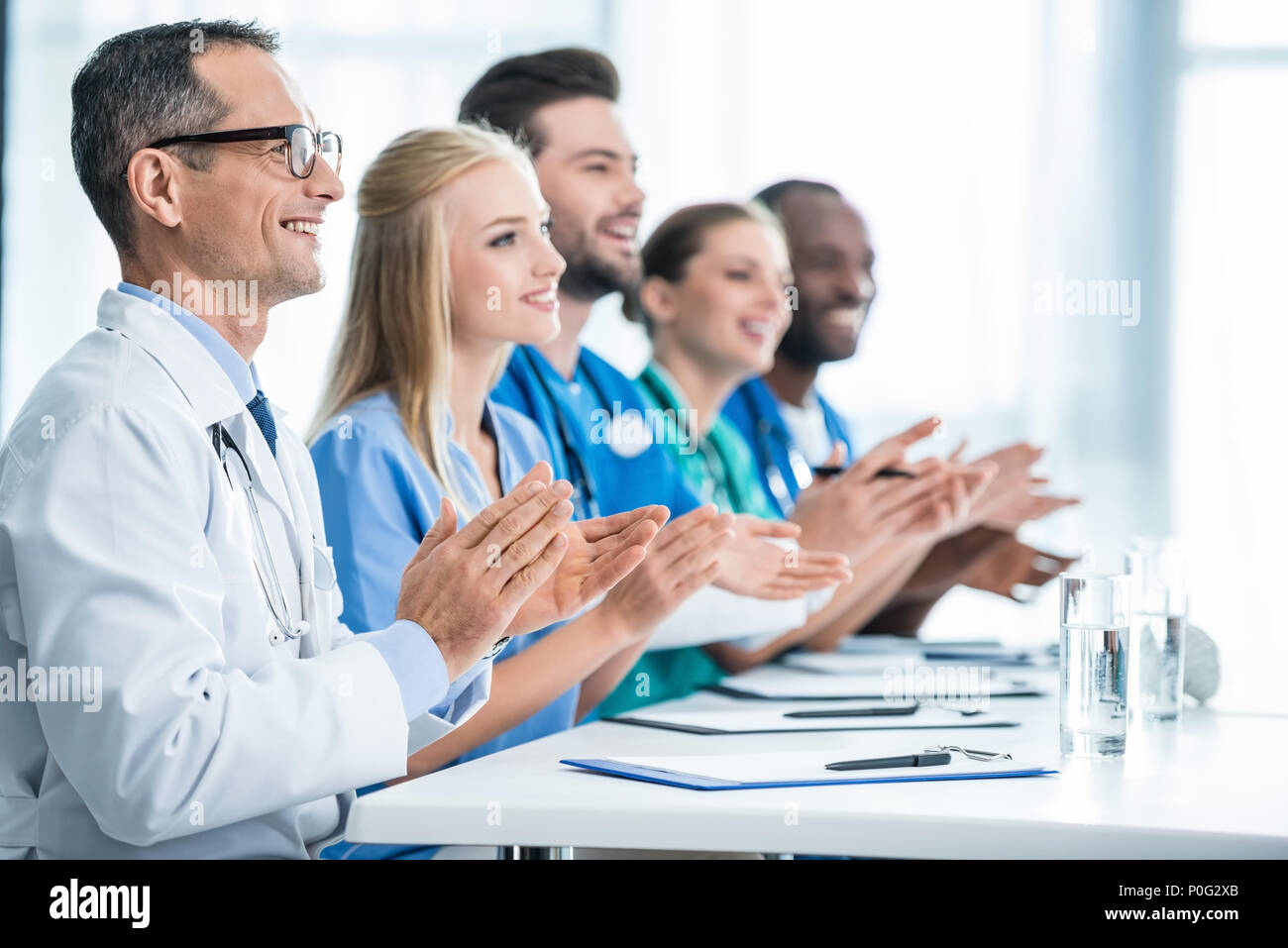 Team di medici seduta a tavola in fila e battendo le mani Foto Stock