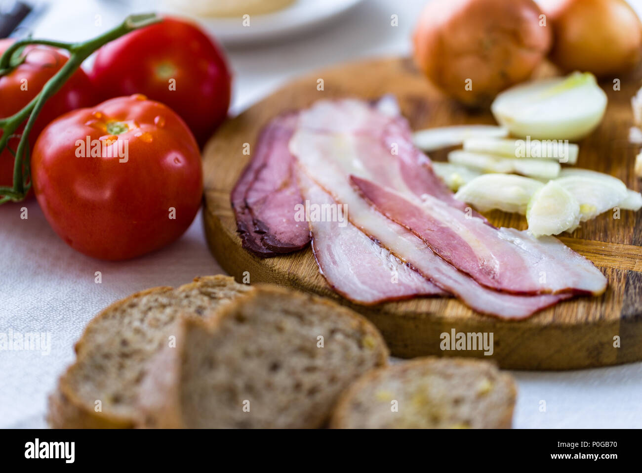 Materie pancetta sul banco di taglio con cipolla e aglio e tomatoe dietro. Foto Stock