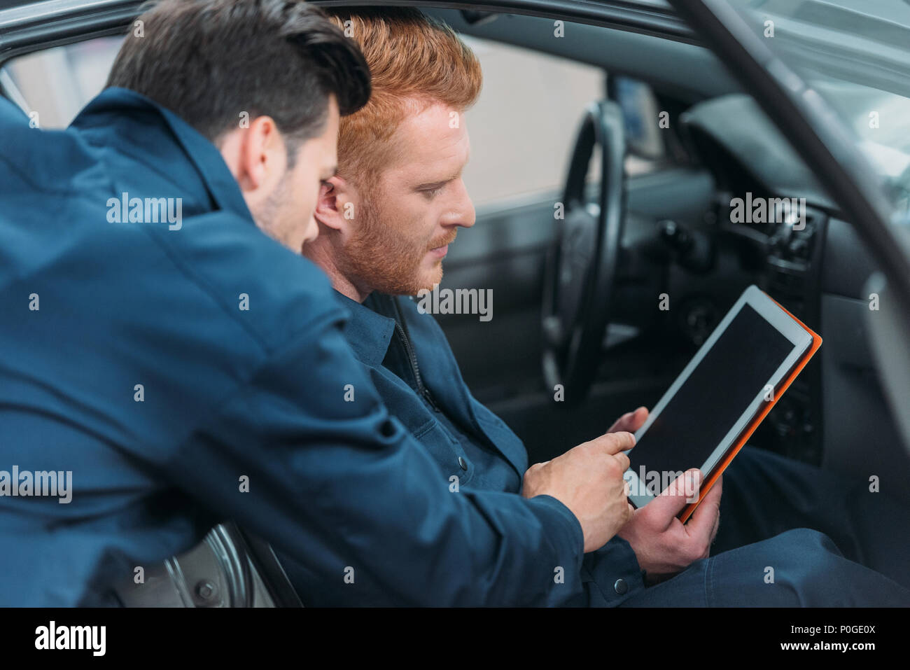 Due meccanici in seduta di una vettura in laboratorio utilizzando una tavoletta digitale. Foto Stock