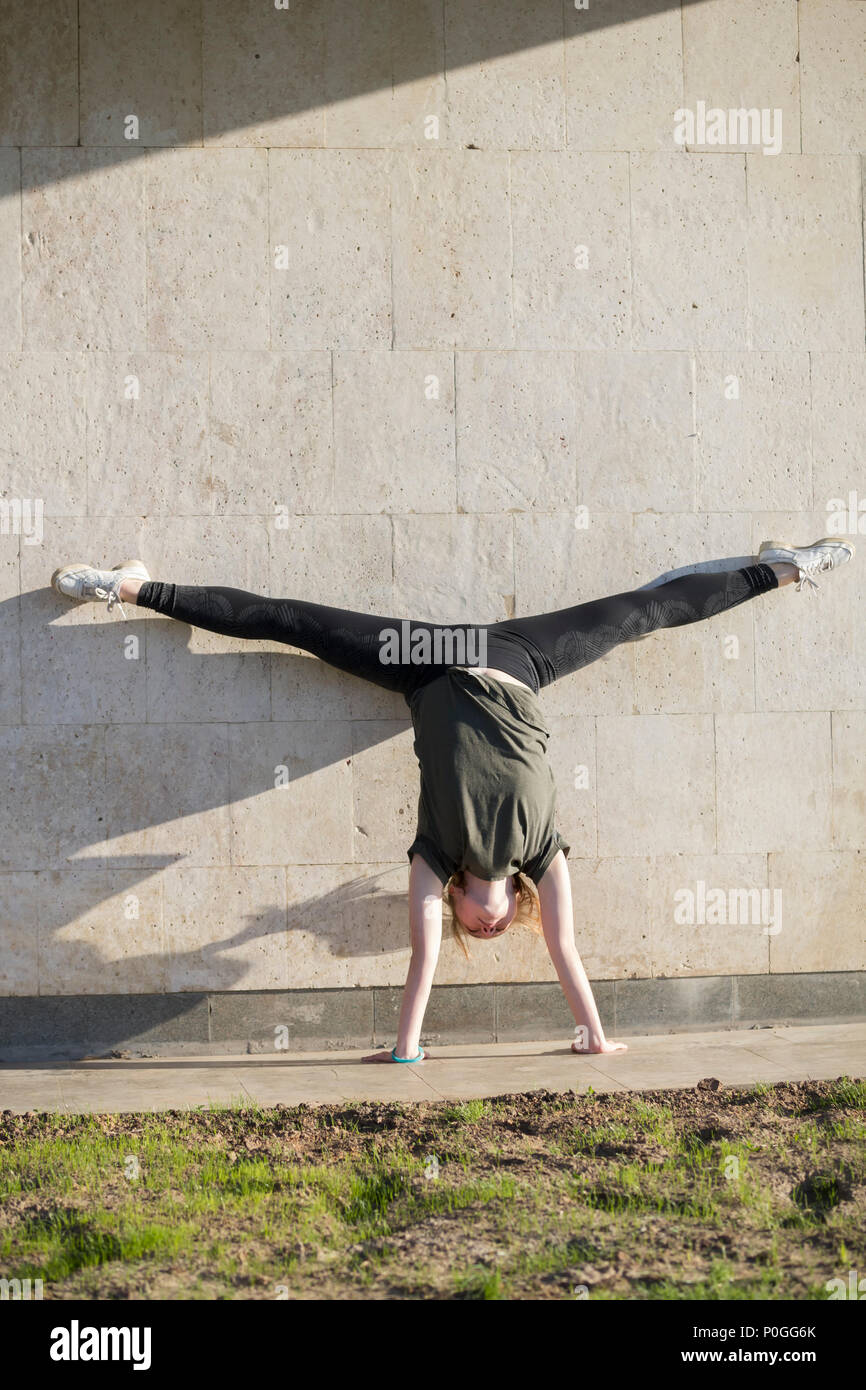 Giovane donna acrobat sul handstand esegue lo spago contro il muro esterno Foto Stock