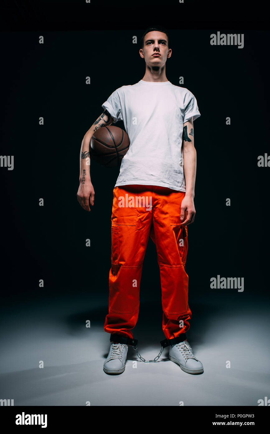 Giovane prigioniero maschio indossa pantaloni arancione e polsini holding  basket ball su sfondo scuro Foto stock - Alamy