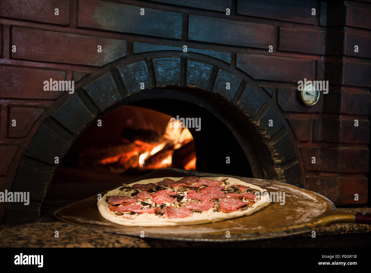 Vista ravvicinata del processo di cottura della pizza cruda sulla stufa di legno  nel forno di mattoni Foto stock - Alamy