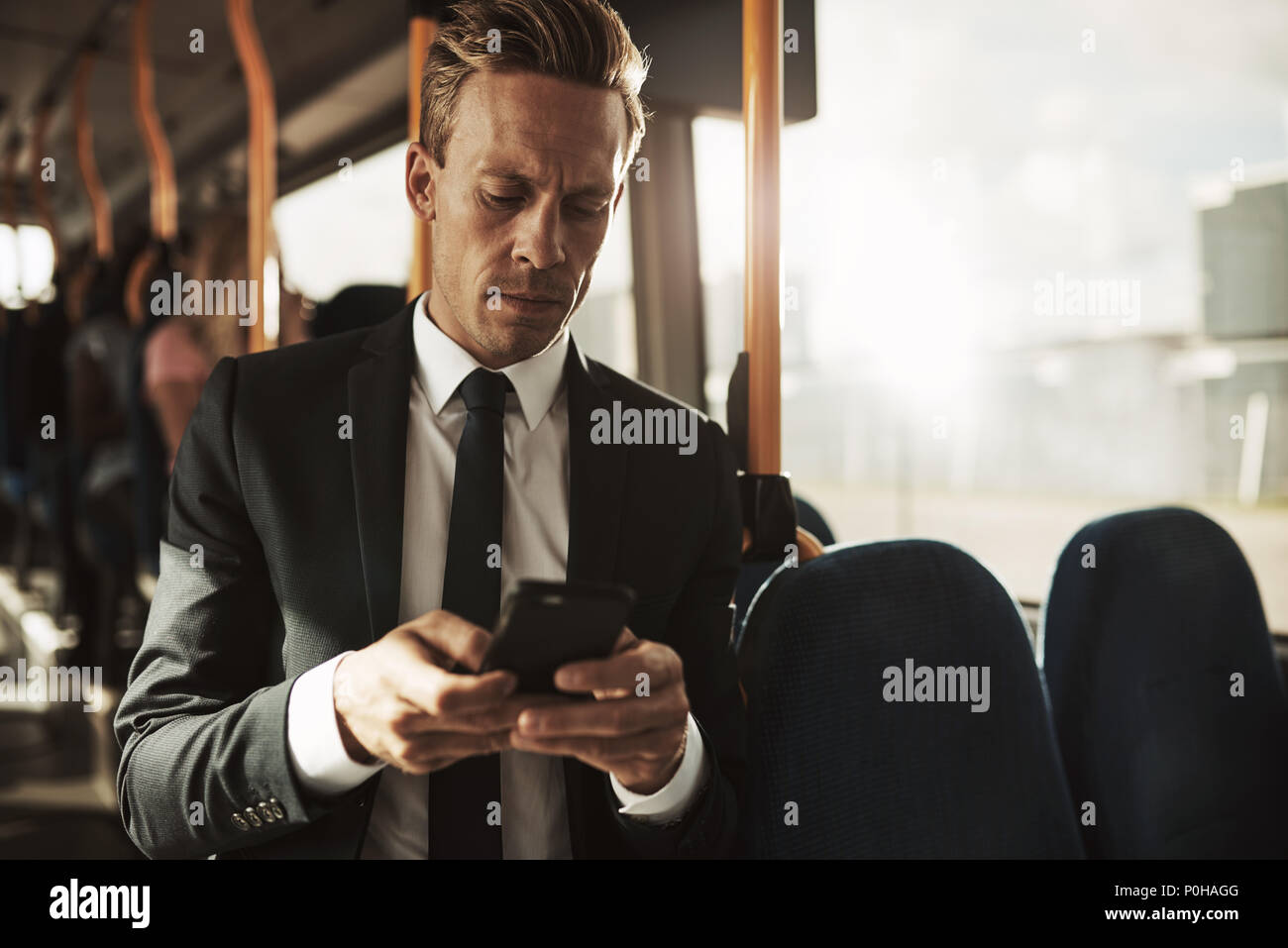 Focalizzato giovane impreditore indossa una tuta in piedi su un bus durante i suoi spostamenti di mattina la lettura di messaggi di testo Foto Stock