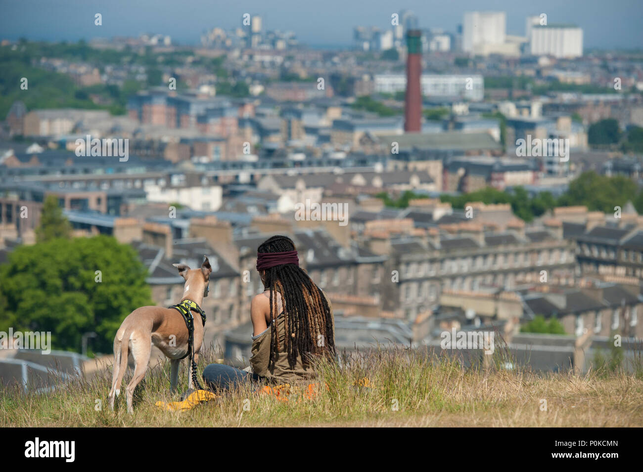 Molto cool, bohemian girl siede nell'erba lunga sulla Carlton Hill in una giornata di sole con Edimburgo al di sotto di lei e il suo cane Foto Stock
