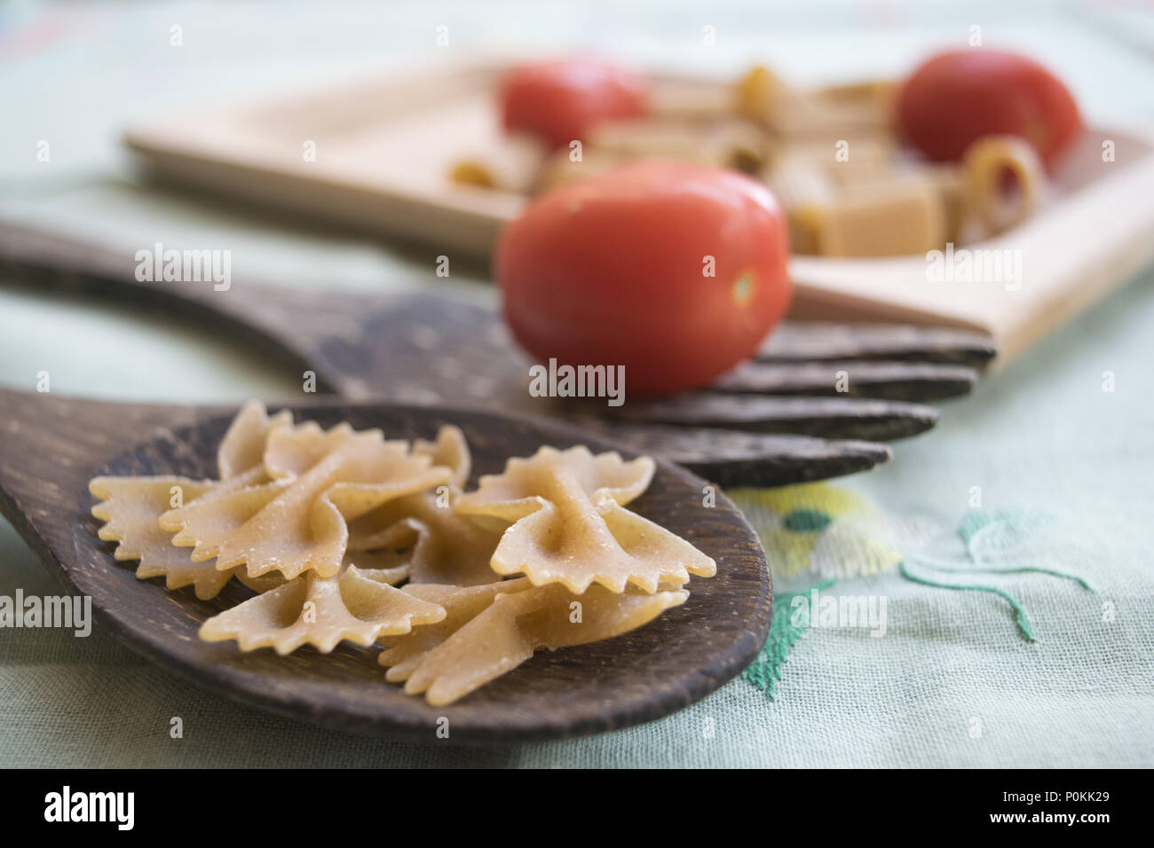 Integrale di farfalle di pasta su un mestolo di legno e freschi pomodori ciliegia Foto Stock