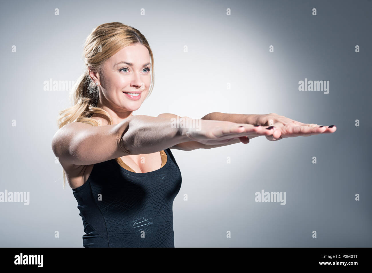 Attraente donna sportive con le mani tese su sfondo grigio Foto Stock