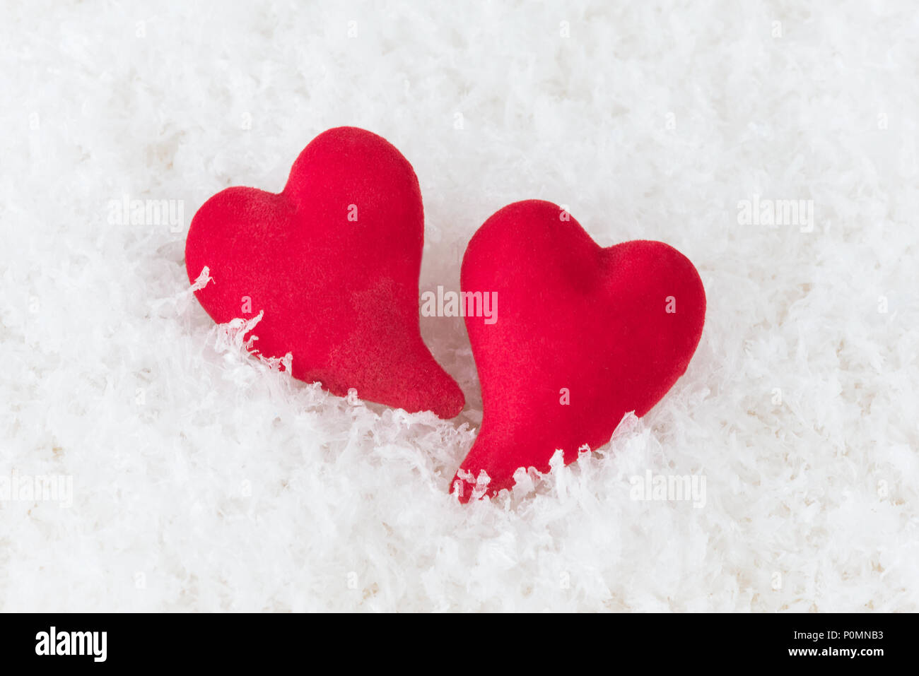 Due cuori rossi giacciono su bianco puffy neve fredda. Metafora dell'amore. Biglietto di auguri per il giorno di San Valentino Foto Stock