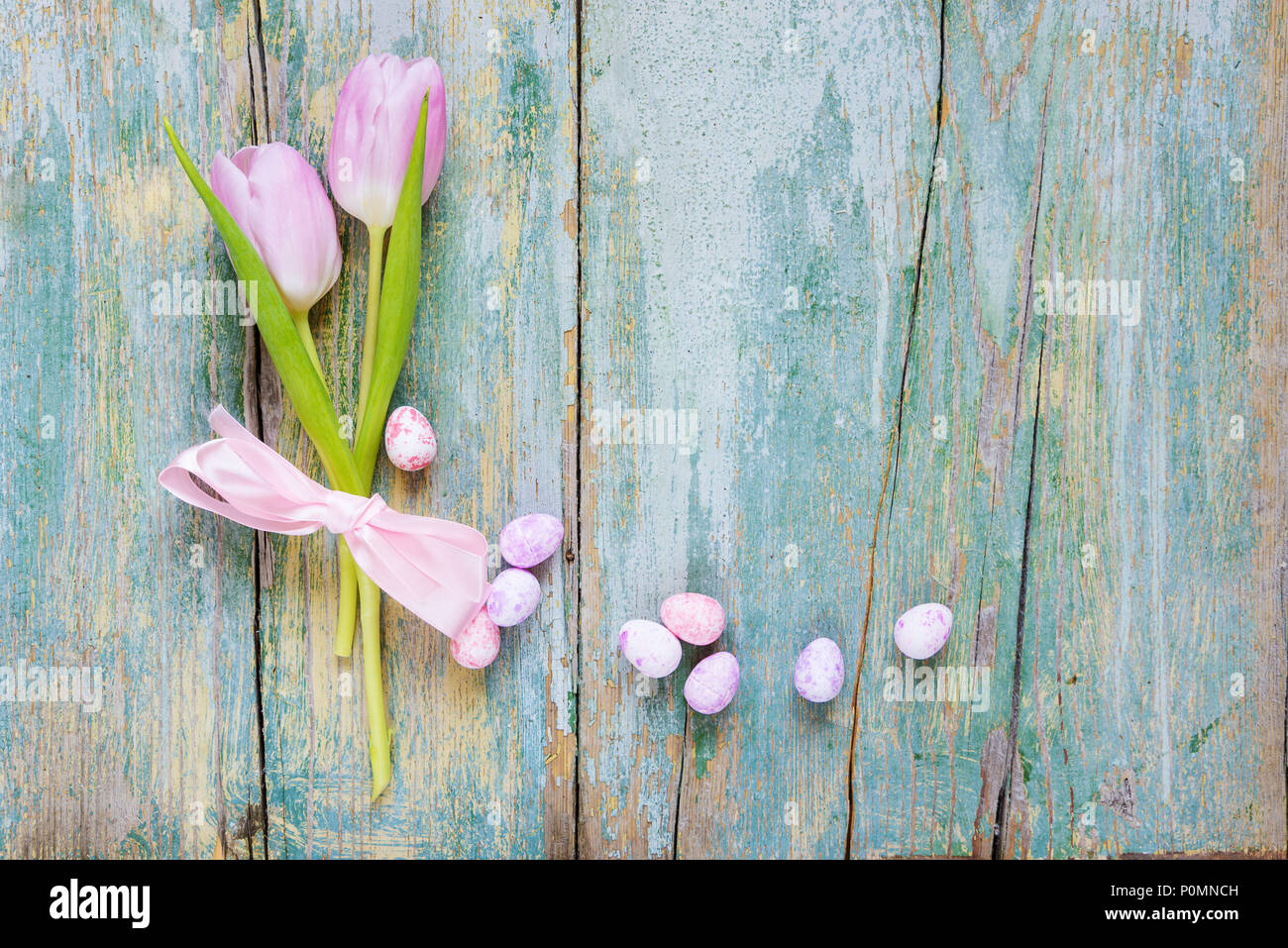 Composizione di pasqua con due pink tulip fiori legati con rosa di nastro di seta, fine dipinto di uova di Pasqua sul vecchio blu sullo sfondo di legno, con copy-spazio, Foto Stock