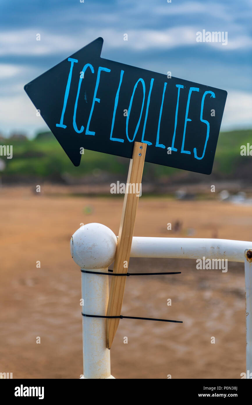 In un giorno caldo, un segno a forma di freccia indica la strada per un ghiaccio venditore per lecca-lecca sulla spiaggia a Bude in North Cornwall Foto Stock