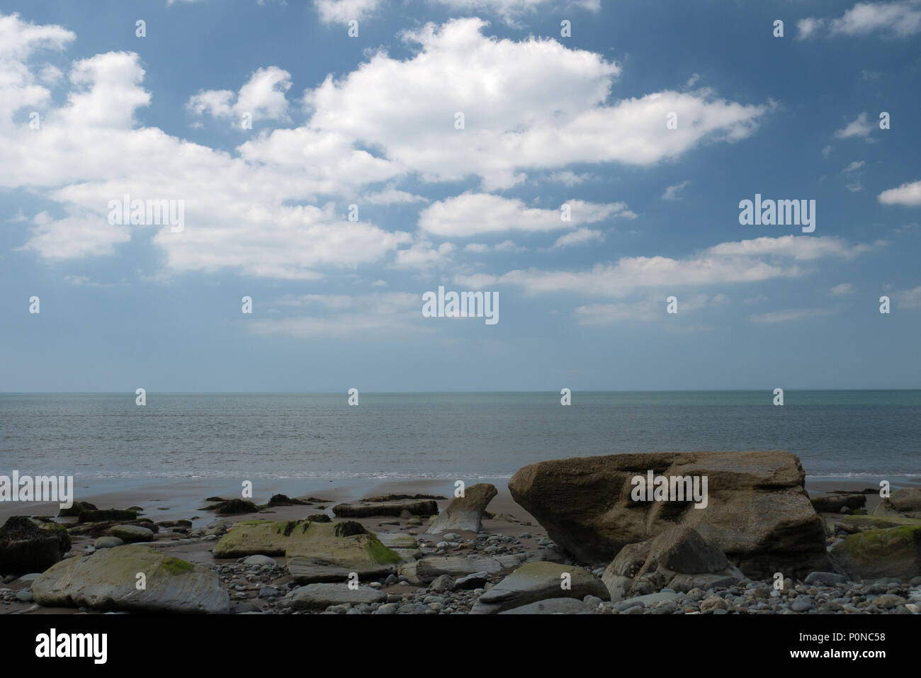 Una calma piatta mare in estate con nuvole bianche su un cielo blu. Foto Stock
