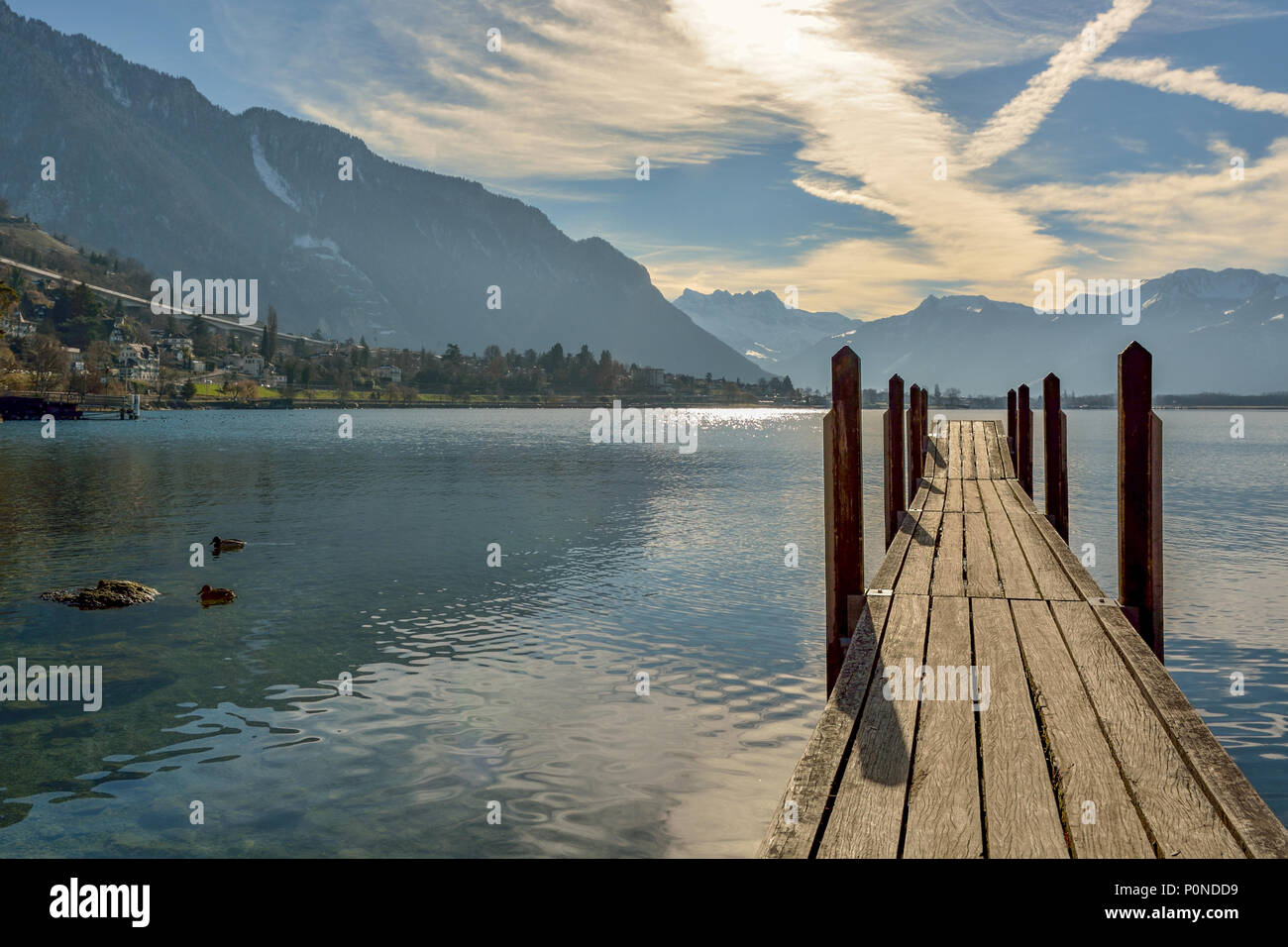 Piccolo molo in legno sul Lago di Ginevra che conduce verso le montagne nevose Foto Stock