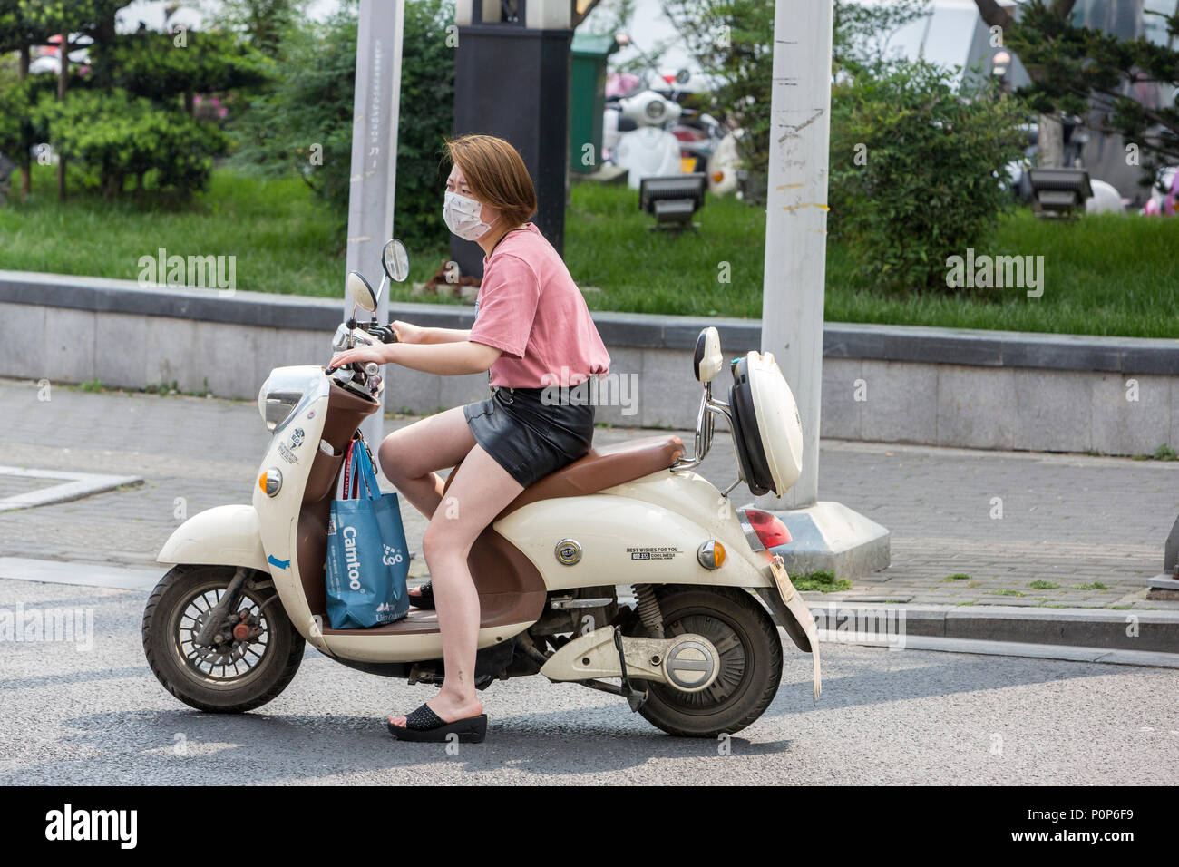 Suzhou, Jiangsu, Cina. Giovane donna cinese con una maschera per la respirazione su una moto. Foto Stock
