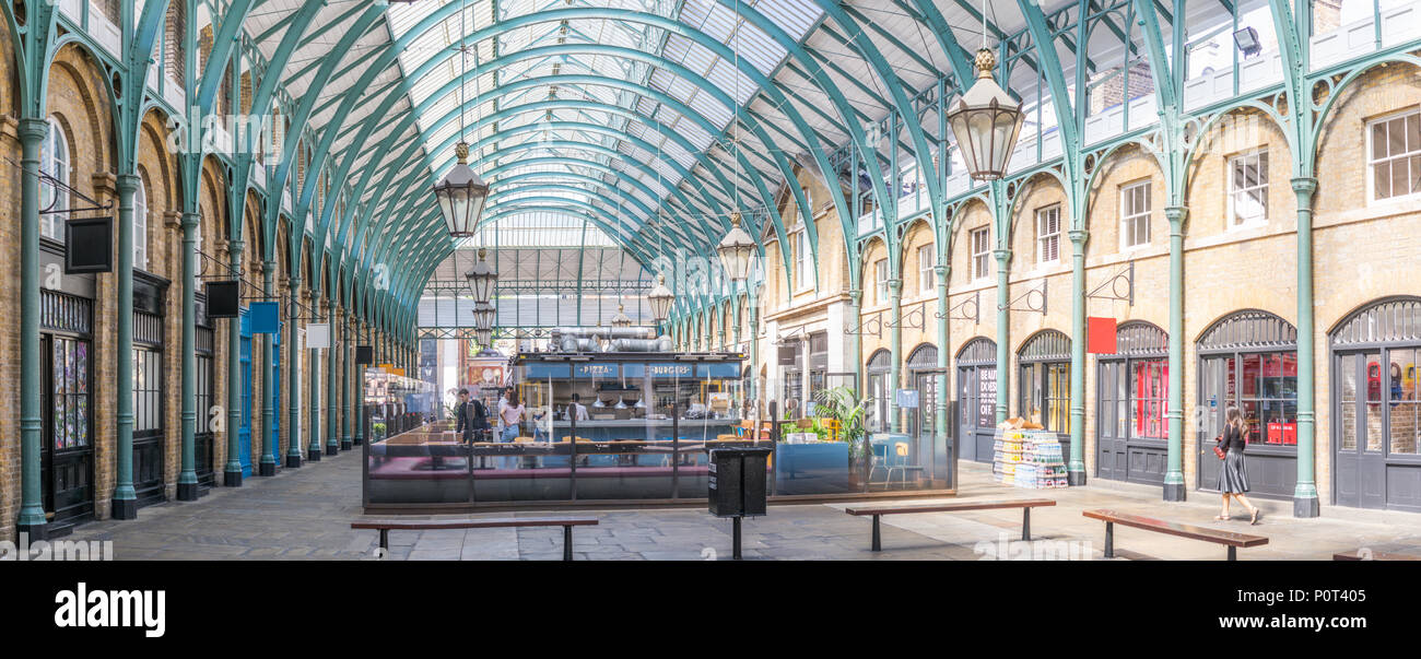Una delle aree aperte al Covent Garden di Londra con il telaio in acciaio verniciato arcate riccamente decorata lampade pendenti verso il basso.i negozi uniformemente posizionati su ciascun lato. Foto Stock