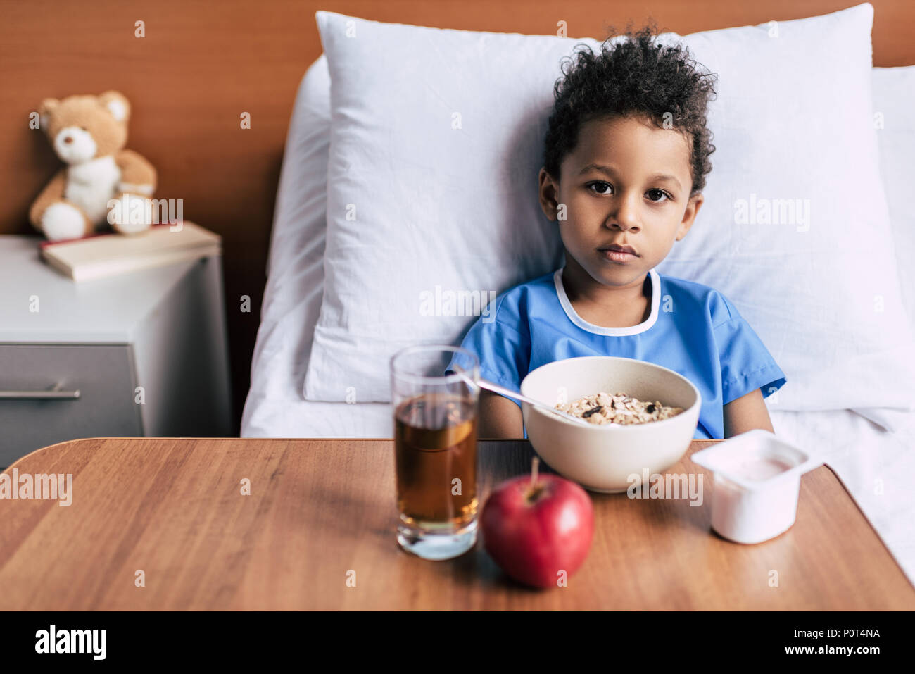 Ritratto di African American Boy con la colazione a tavola di piccole dimensioni sul letto guardando la fotocamera in clinica Foto Stock