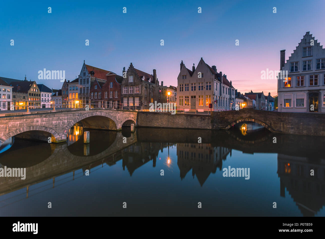 Le luci del tramonto su edifici storici del centro città si riflette nei tipici canali di Bruges Fiandre Occidentali Foto Stock