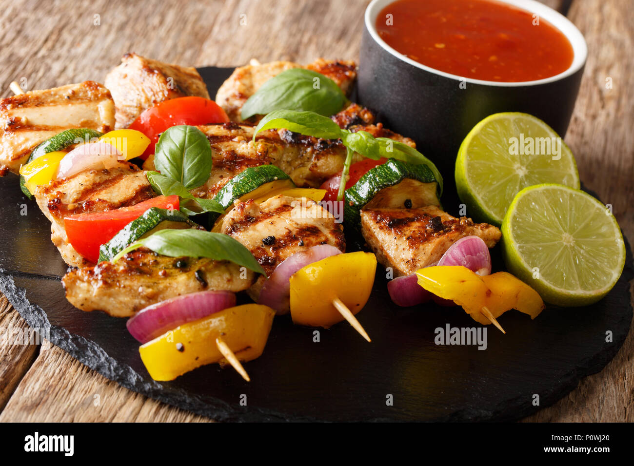 Grigliate gli spiedini di pollo con verdure estive con salsa, basilico e calce closeup sul tavolo orizzontale. Foto Stock