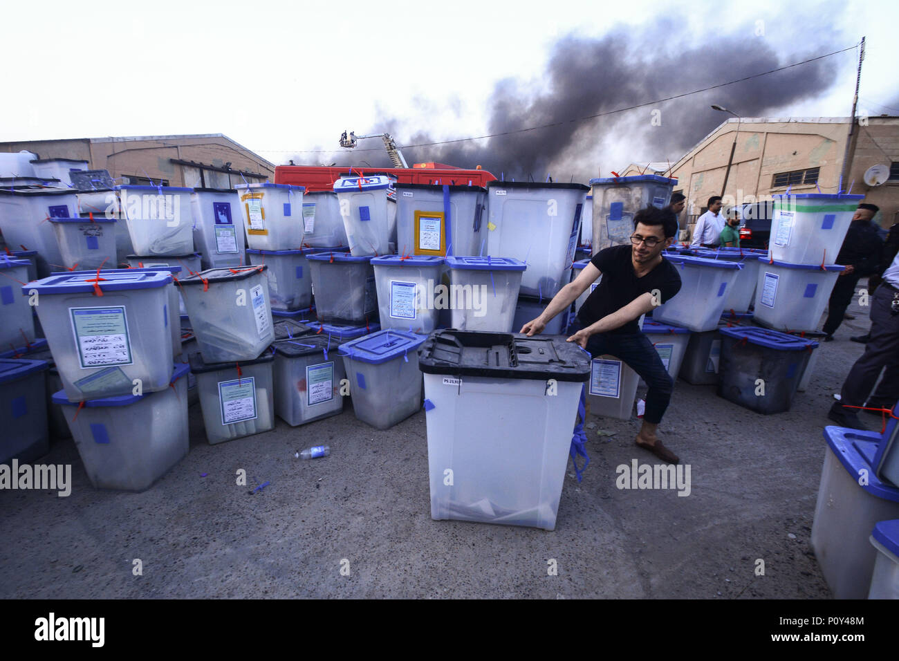 Baghdad in Iraq. Decimo Giugno, 2018. Un uomo si muove un urne come il fumo aumenta da un incendio scoppiato a Baghdad la più grande scrutinio magazzino a Baghdad, Iraq, 10 giugno 2018. L'Iraq e il Parlamento ha votato Mercoledì a favore di una votazione a scrutinio manuale raccontano in mezzo alle accuse di frode. Credito: Ameer Al Mohammedaw/dpa/Alamy Live News Foto Stock