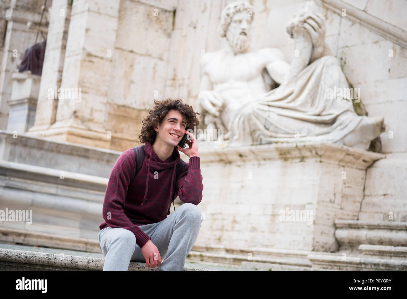 Bel giovane con capelli ricci in tuta di parlare sul suo telefono mobile nella parte anteriore del dio Nilo statua in Roma Foto Stock