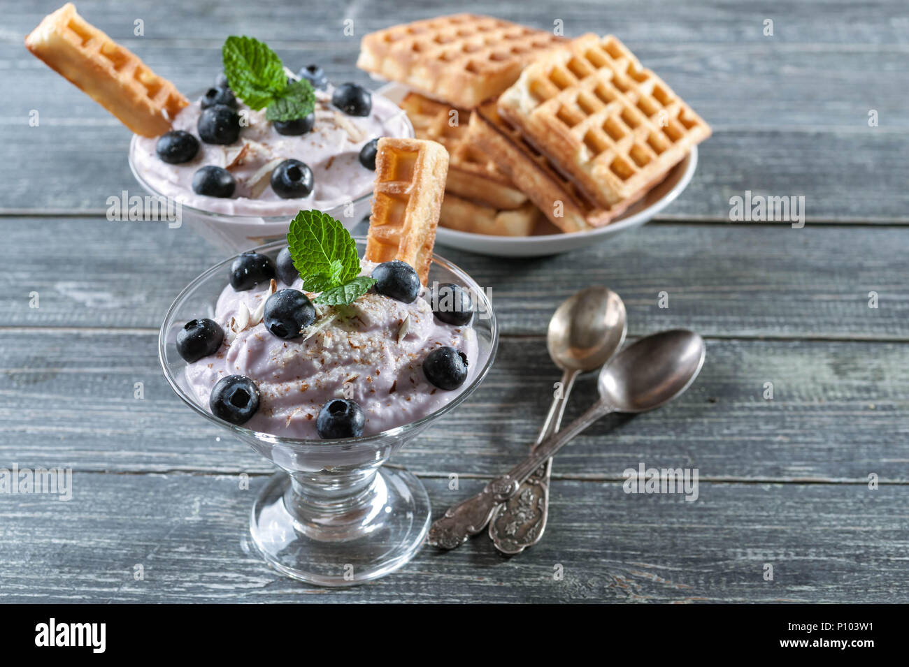 Ricotta dolce con i mirtilli in un bicchiere di vetro e in Casa Viennese di cialde su uno sfondo di legno Foto Stock