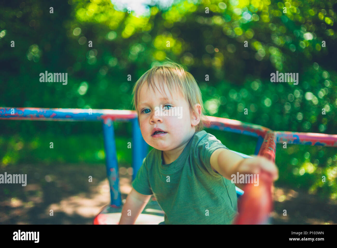 Un grazioso piccolo ragazzo è seduto su un merry-go-round nel parco Foto Stock