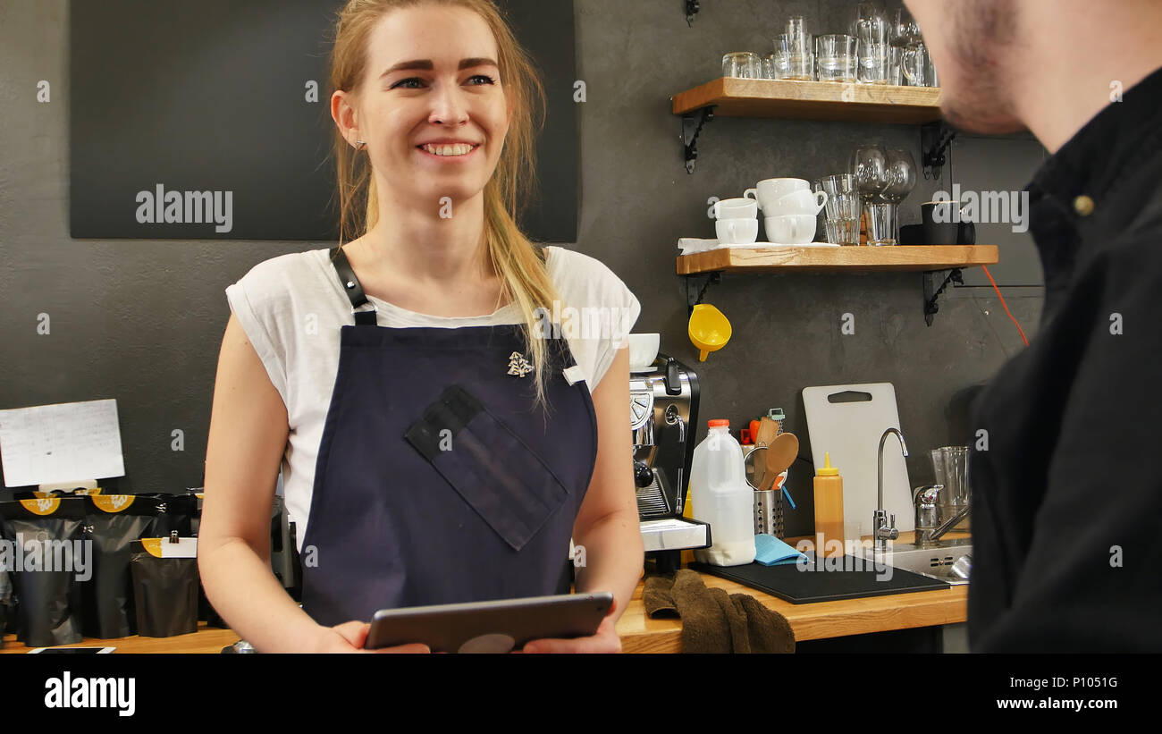 Ritratto di una bellissima femmina barista prendendo l'ordine di un cliente con un computer tablet e sorridente Foto Stock