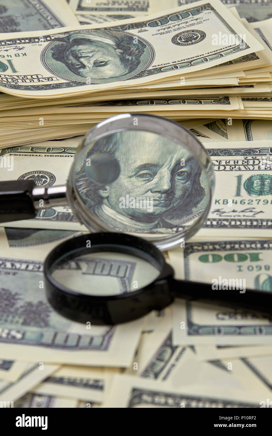 Pila di banconote da cento dollari con lenti di ingrandimento. Lente di ingrandimento si trova in dollari americani. Foto Stock