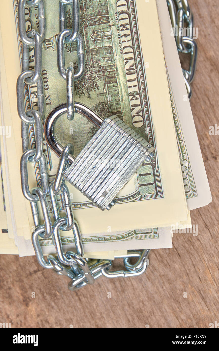 Centinaia di dollari di banconote è fissato con una catena e un lucchetto. Close up. In legno marrone dello sfondo. Foto Stock