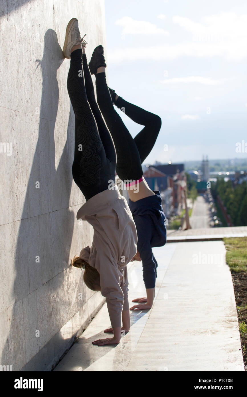 Due giovani donne acrobat facendo handstand sulla parete con il paesaggio sullo sfondo Foto Stock