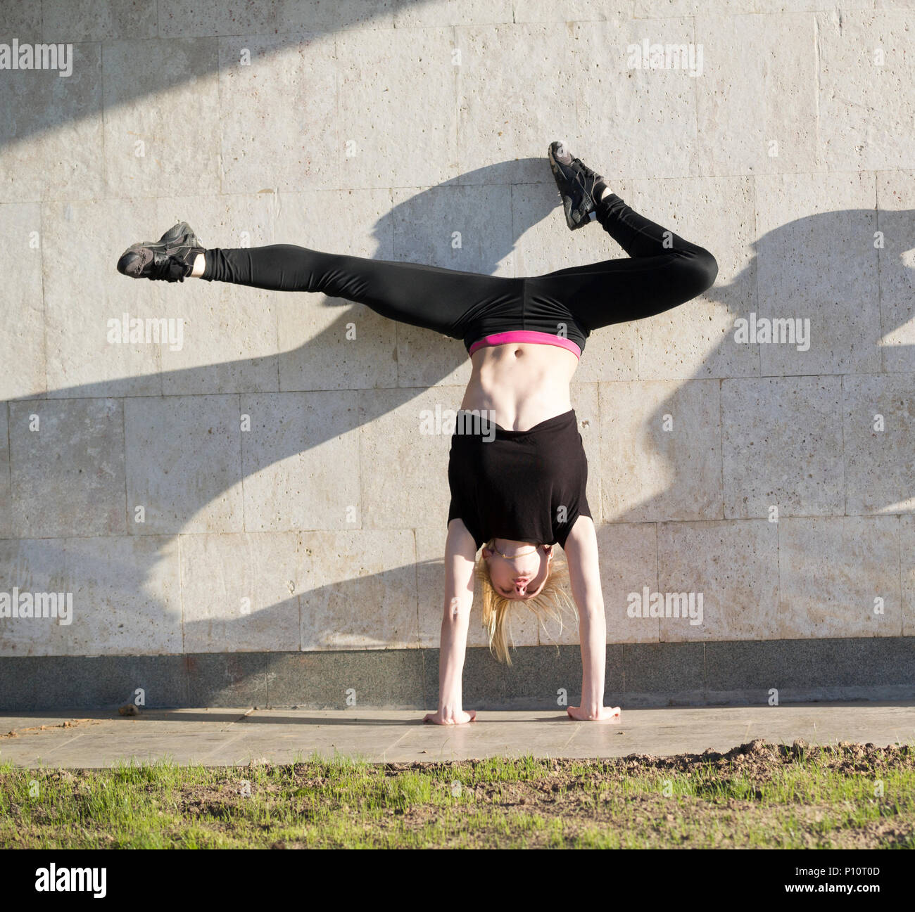 Giovane donna acrobat sul handstand esegue lo spago contro il muro esterno Foto Stock