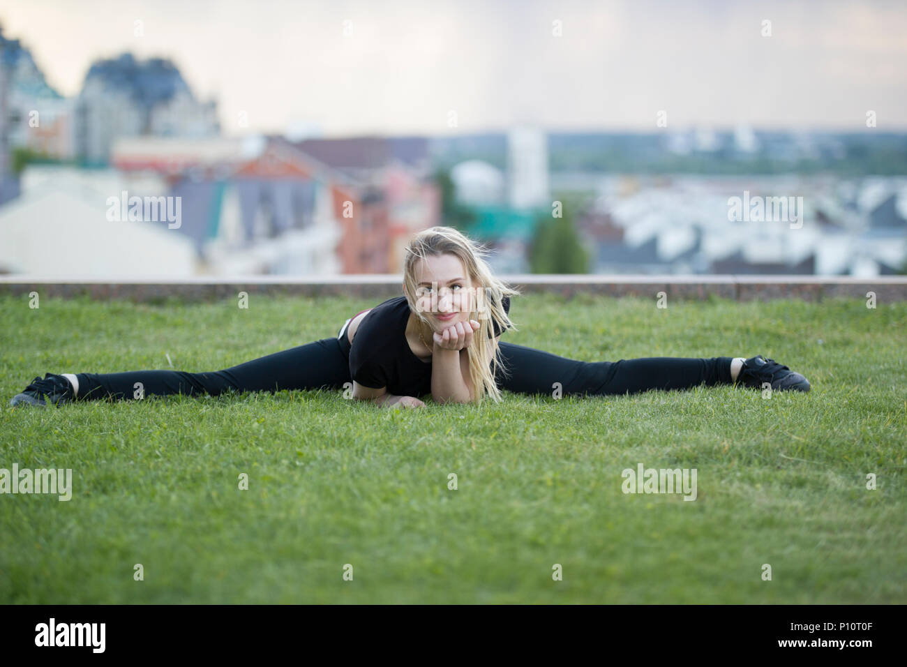 Sorridente ragazza sull'erba verde esegue la legatura a spago, sul paesaggio urbano di sfondo Foto Stock