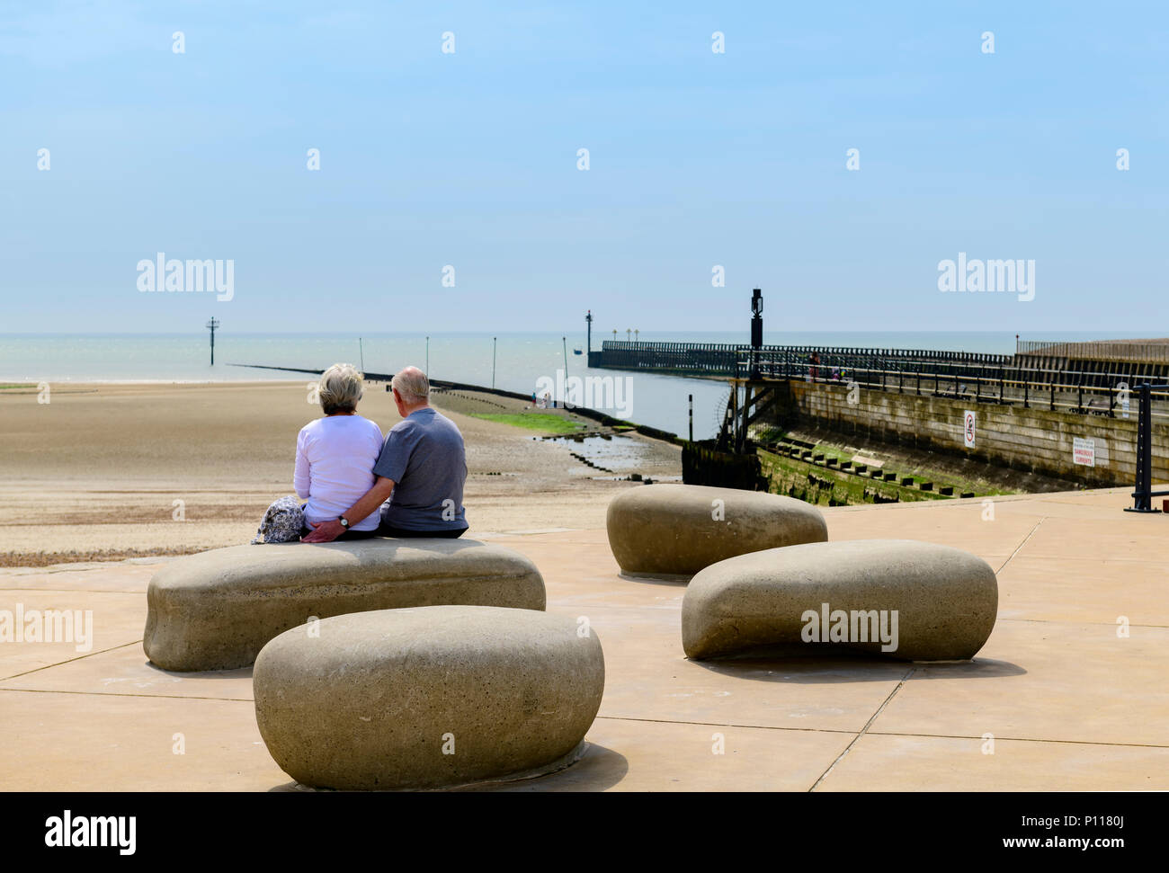 Vista posteriore della coppia di anziani seduti su alcuni grandi pietre che guarda al mare Foto Stock