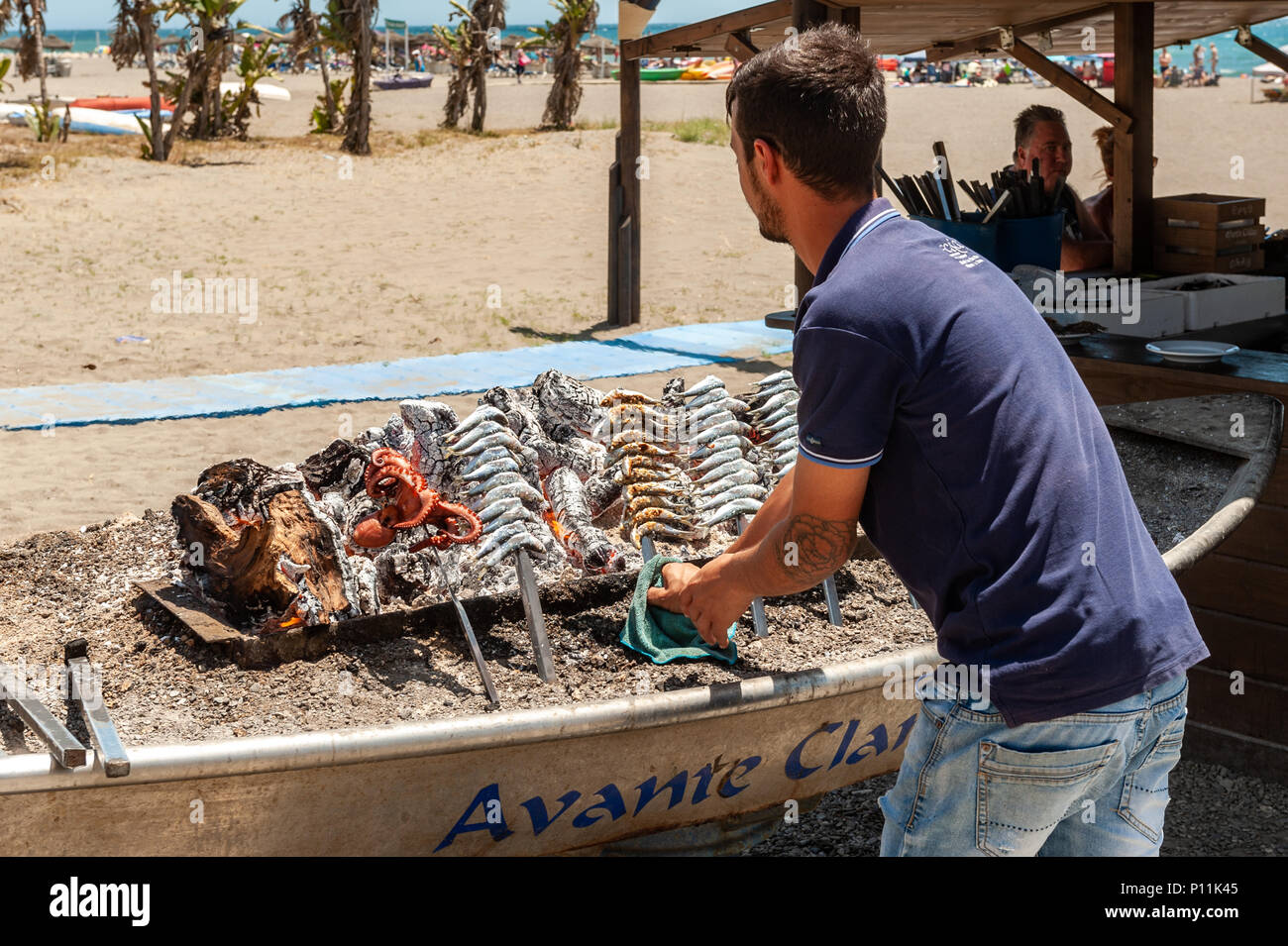L'uomo la cottura di sardine e polpo su un barbecue sulla spiaggia di Malaga, Axarquía, la Cala del Moral comune di Rincón de la Victoria, Malaga, Spagna Foto Stock