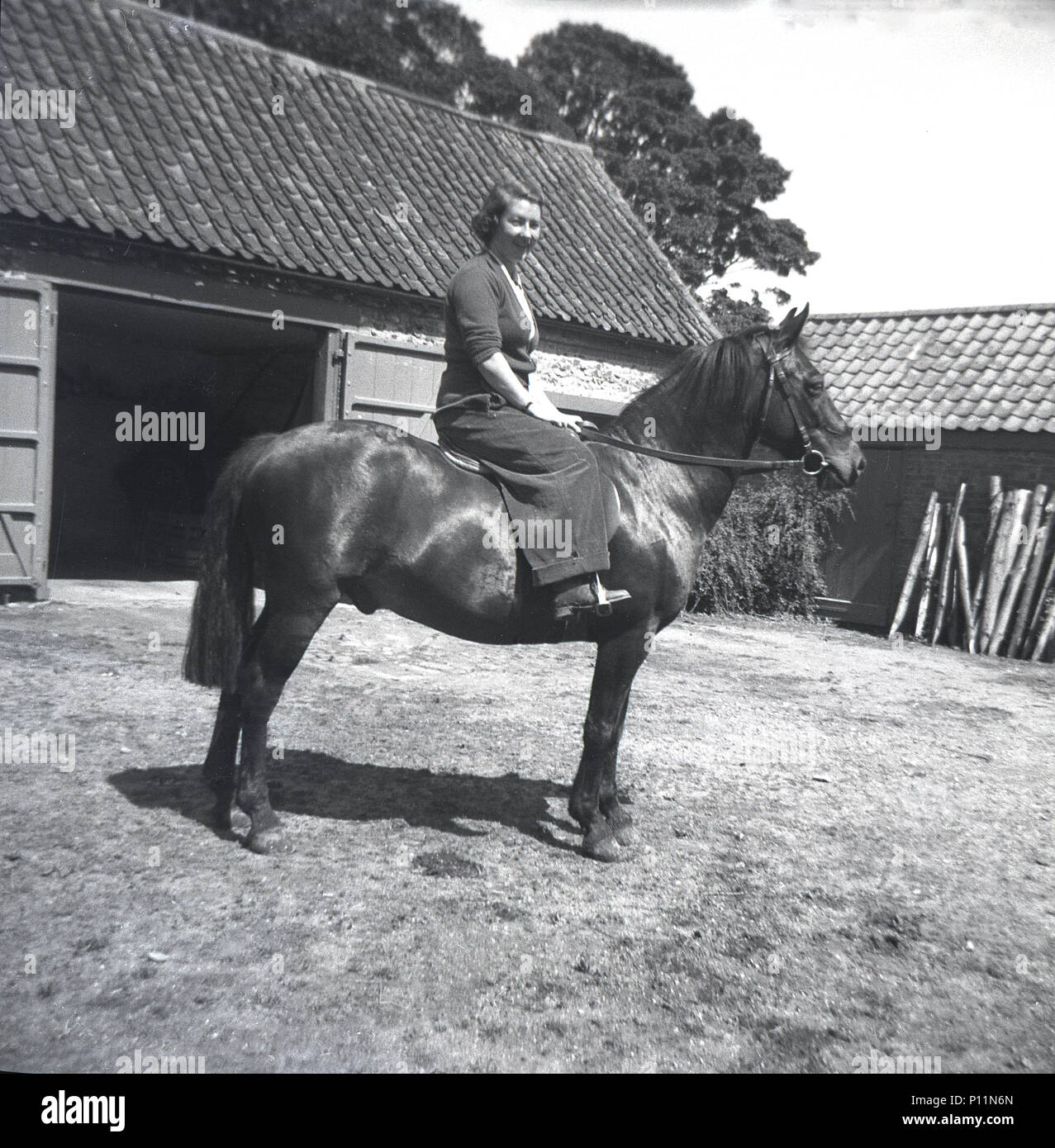 1951, storico, giovane donna seduta su un cavallo nel cortile di una fattoria, Inghilterra, Regno Unito. Foto Stock