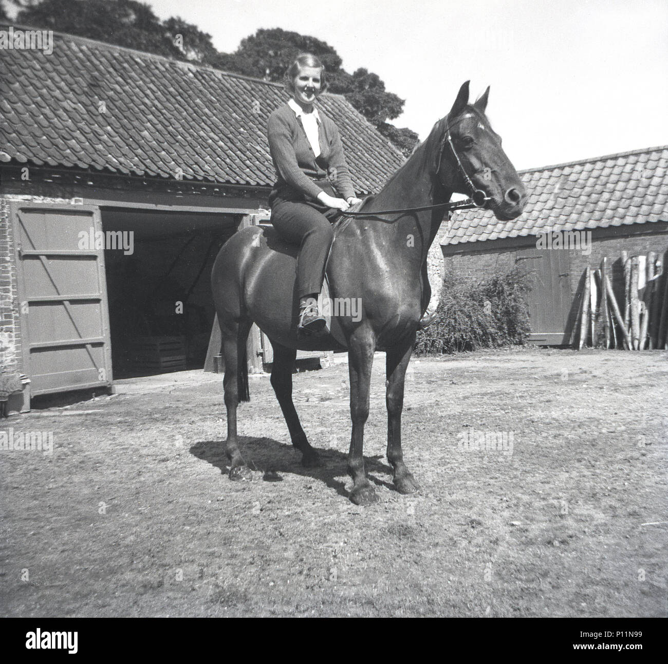 1951, storico, giovane donna seduta su un cavallo al di fuori di una stabile in un cortile, Inghilterra, Regno Unito. Foto Stock