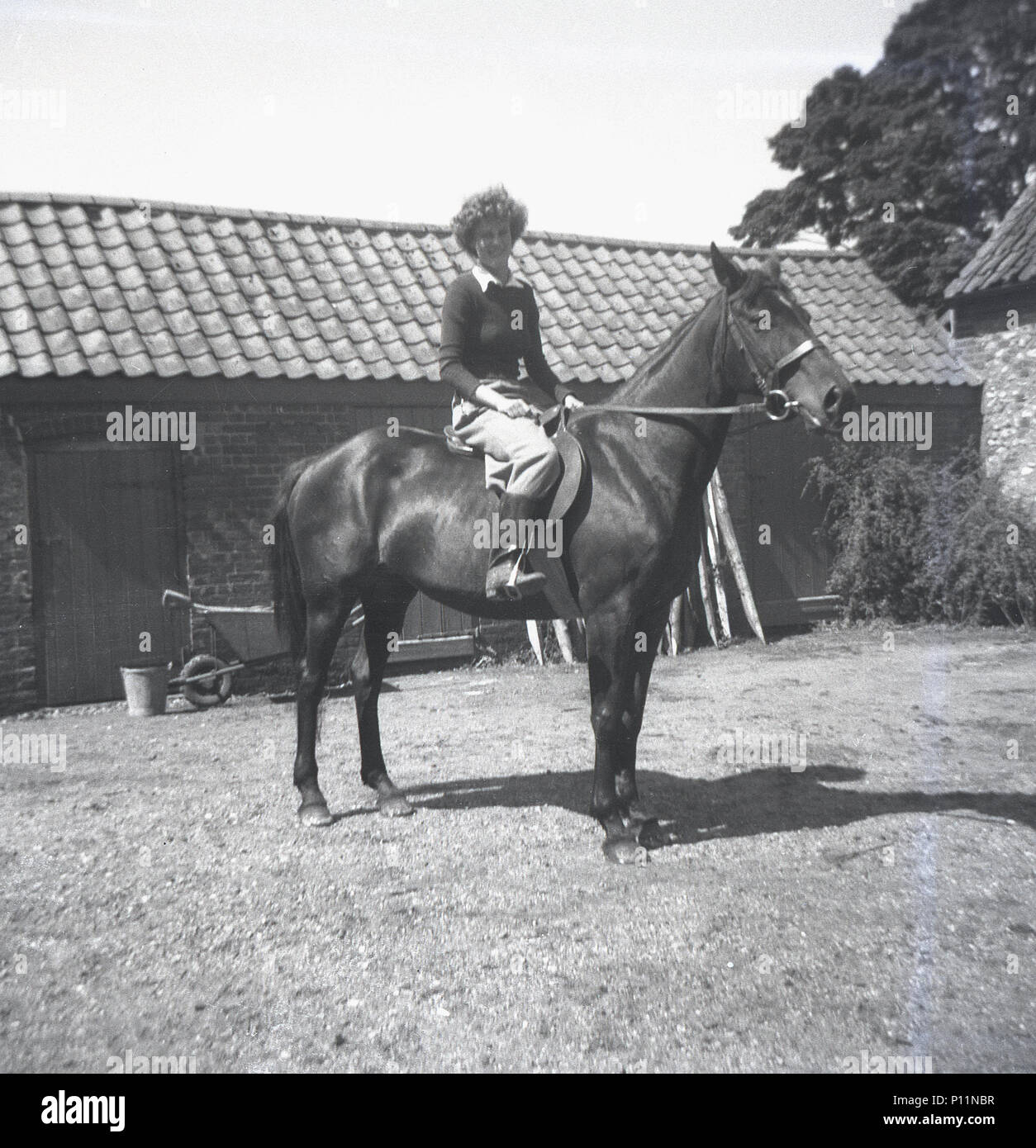 1951, storico, giovane donna seduta su un cavallo al di fuori di una stabile in un cortile, Inghilterra, Regno Unito. Foto Stock
