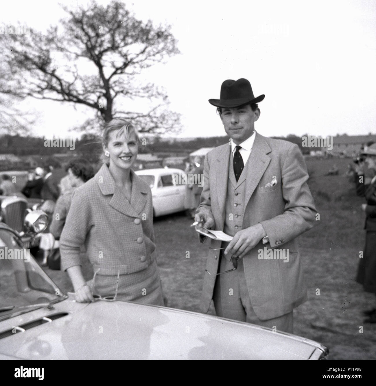 1958 maggio, una giovane signora e un giovane gentiluomo ben vestita con un abito a tre pezzi, un cappello e una sigaretta e una racecard in mano, si riuniscono in un incontro di corse di cavalli amatoriali da punto a punto a Penshurst, Edenbridge, Inghilterra, Regno Unito. Foto Stock