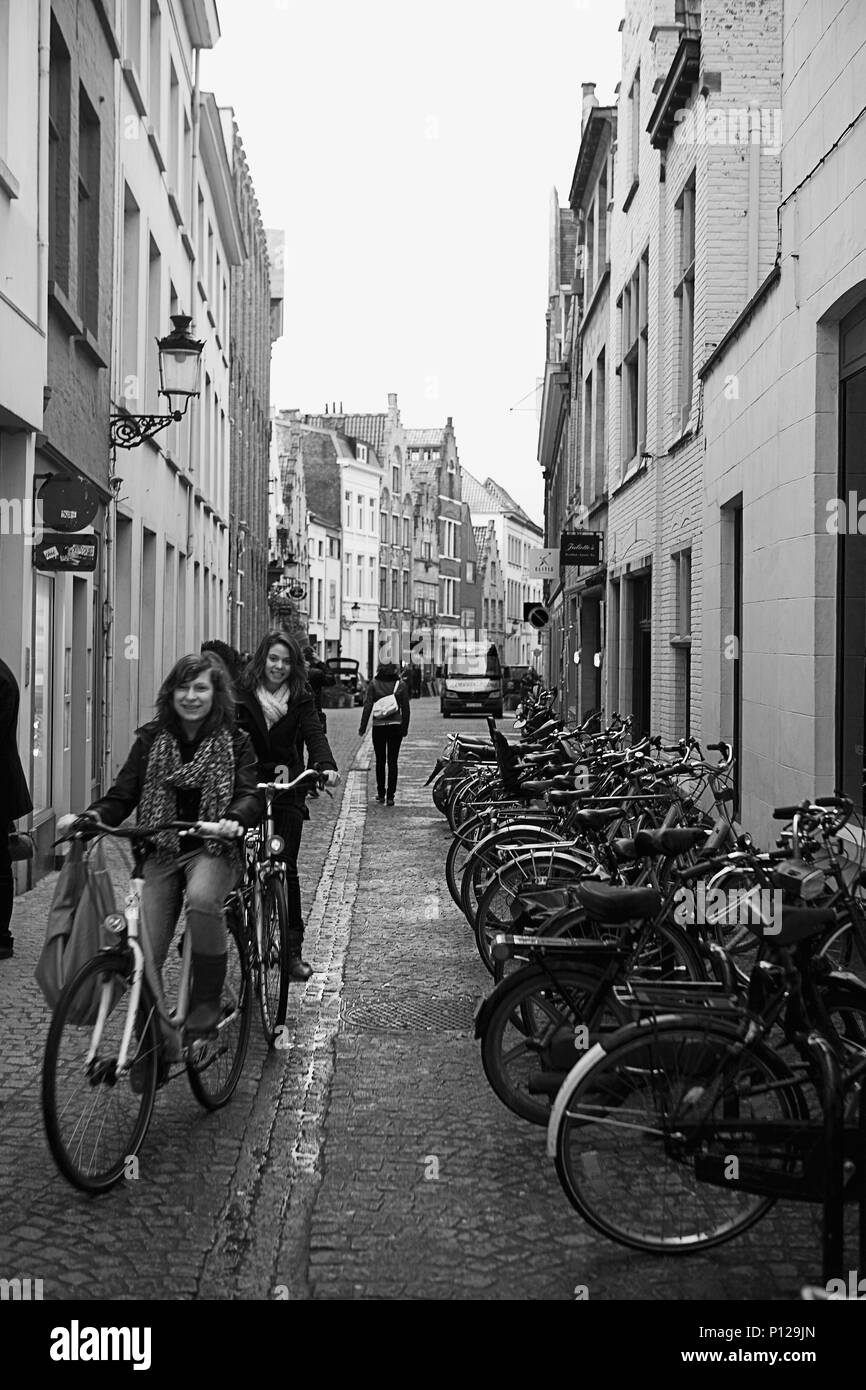 Dweerstraat, Brugge, Belgio: Due ragazze sorridenti verso il basso del ciclo di una corsia di ciottoli: versione in bianco e nero Foto Stock