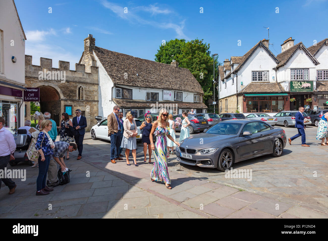 Gli ospiti dei matrimoni e damigelle in piazza del mercato dopo un matrimonio in Malmesbury Abbey, Wiltshire, Regno Unito Foto Stock