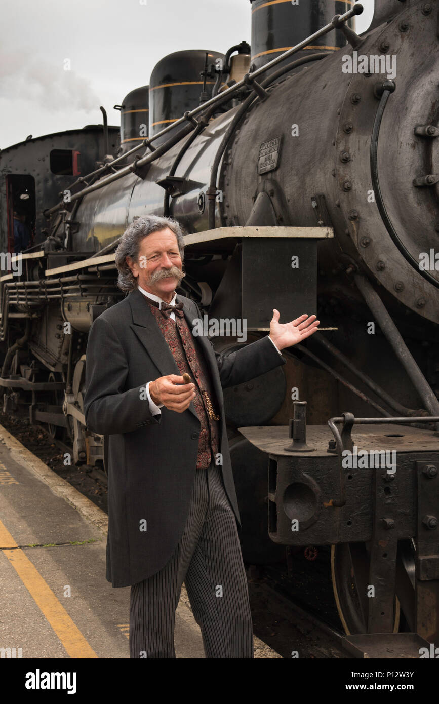 Una guida turistica, vestito come Mark Twain, pone accanto a un treno a vapore in Essex Connecticut Foto Stock